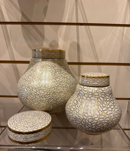 Three white crackle-glazed ceramic jars with gold rims on a glass shelf.