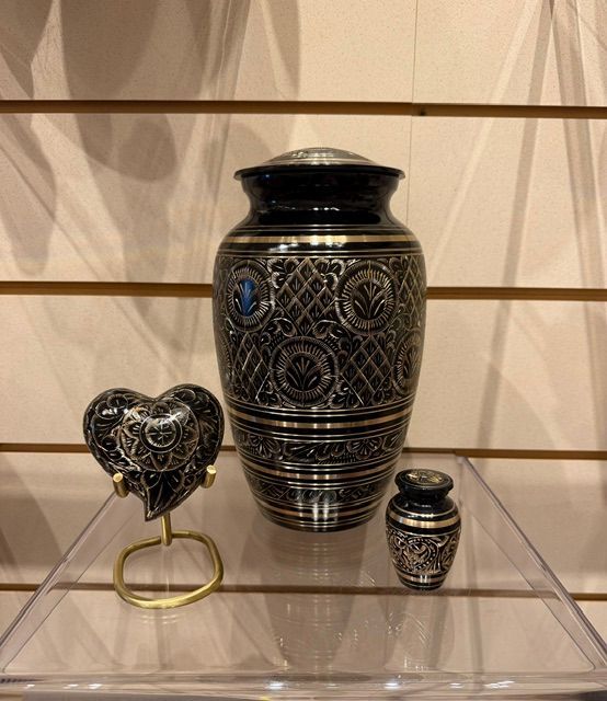 Decorative black and silver urn with matching small jar and heart-shaped ornament on a display shelf