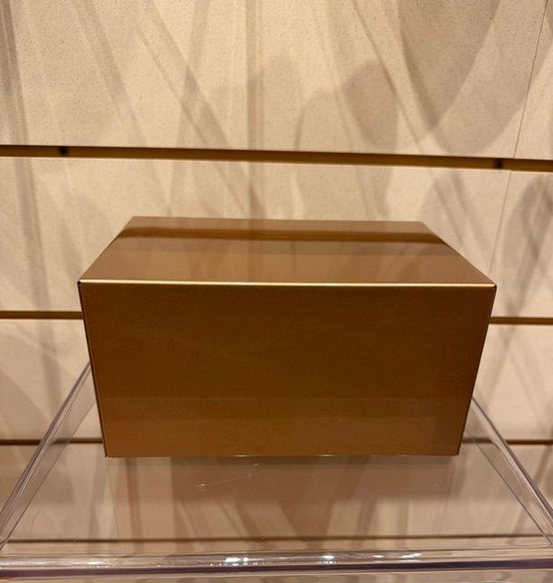 Brown rectangular box displayed on a clear acrylic shelf against a beige wall with shadowed lines