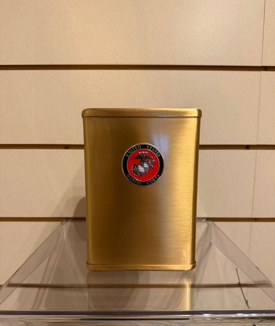 Gold metal canister with a red circular logo, displayed on a clear shelf against a slatted wall.