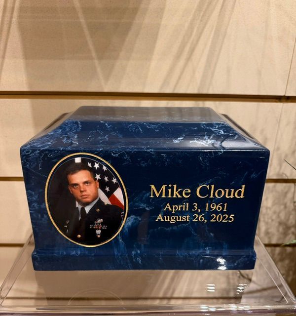 Blue memorial urn engraved “Mike Cloud” with dates, and a portrait medallion on a clear stand.