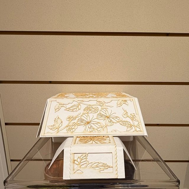 Decorative white lamp with gold floral patterns inside a clear pyramid display case