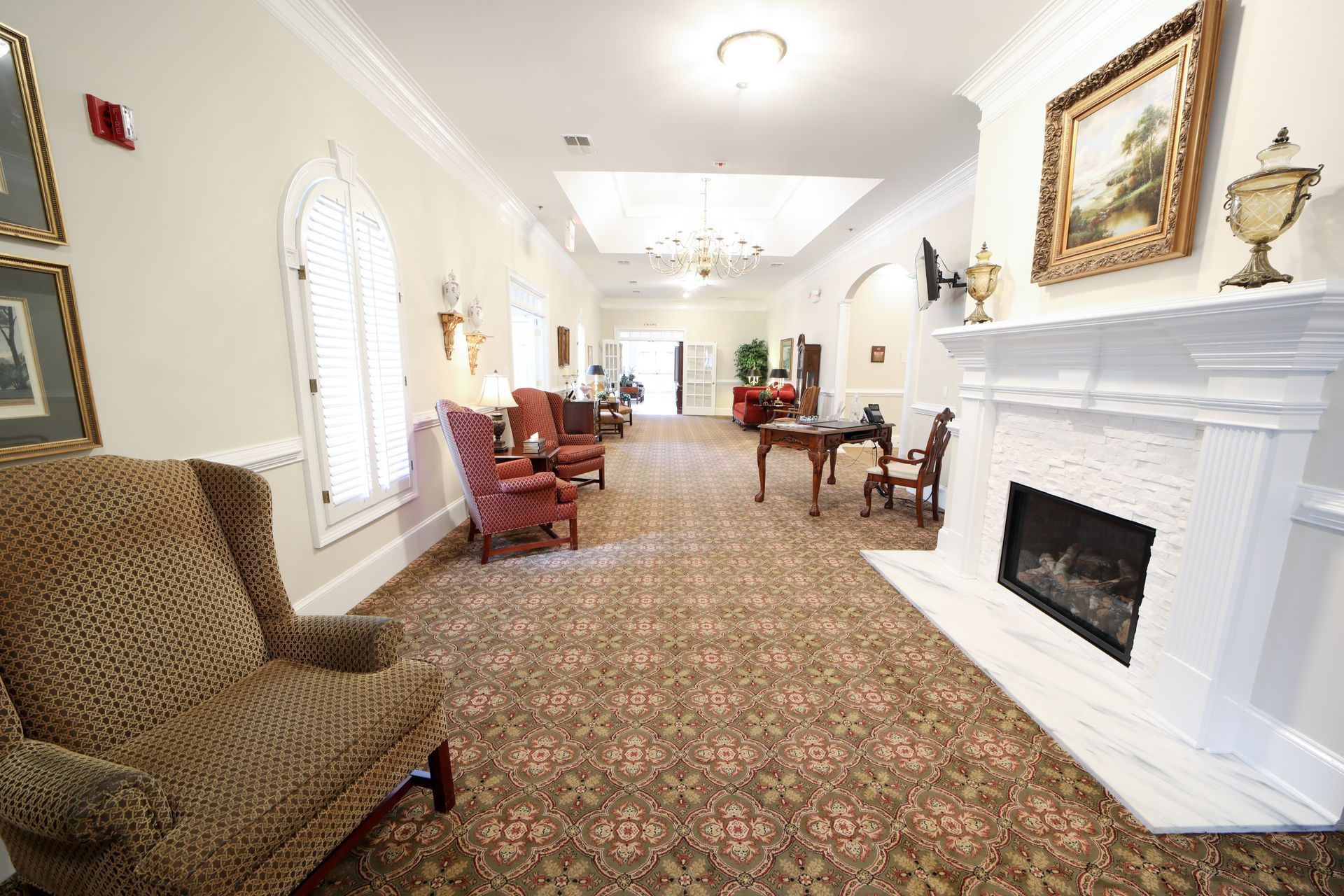 Bright elegant lounge with patterned carpet, white fireplace, red chairs, and large windows