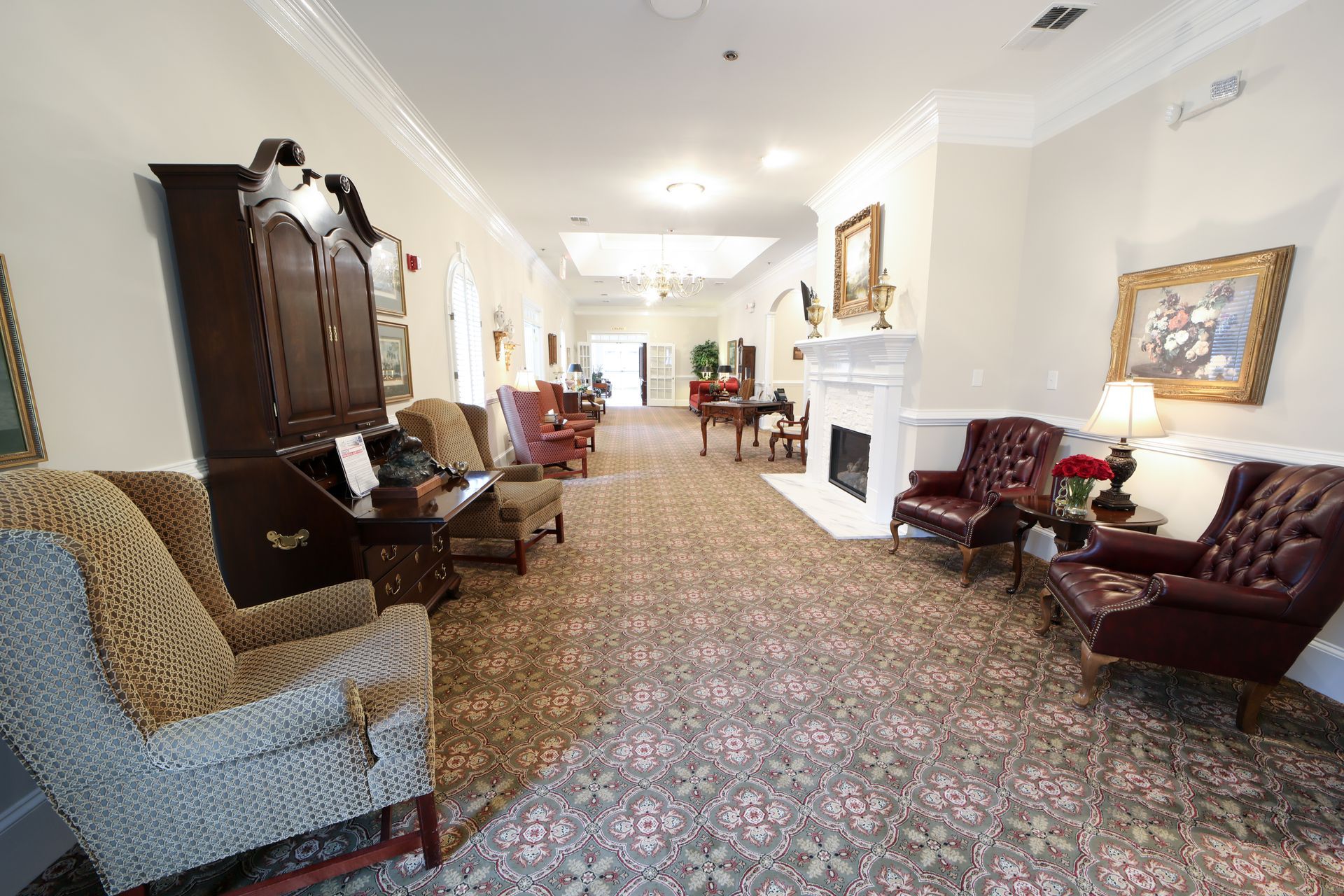 Elegant lounge with patterned carpet, fireplace, upholstered chairs, and antique furniture in a bright hallway