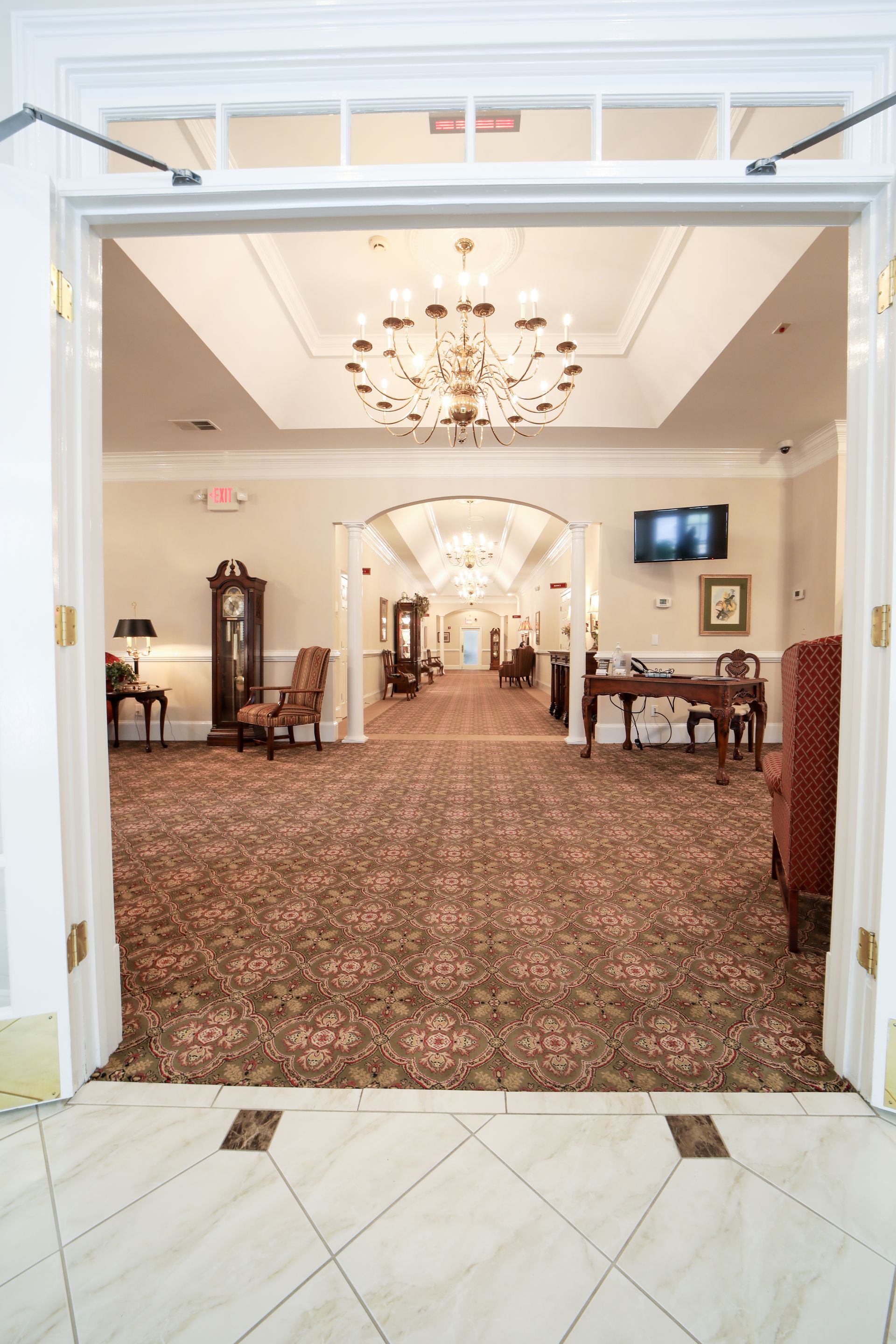 Elegant hotel lobby with patterned carpet, chandeliers, and seating area viewed through open double doors