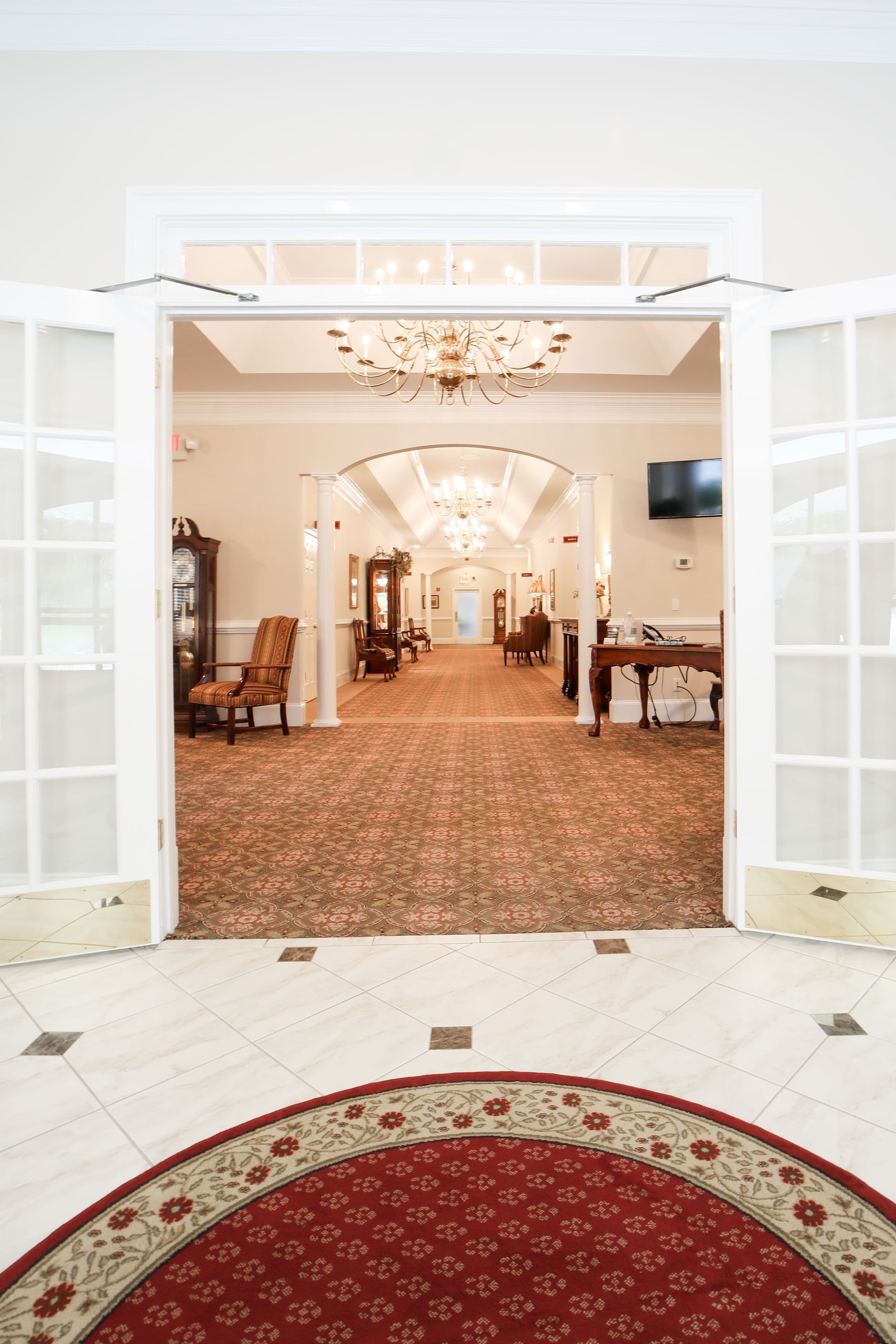 Grand entrance to an elegant banquet hall with red carpet, chandeliers, and open French doors