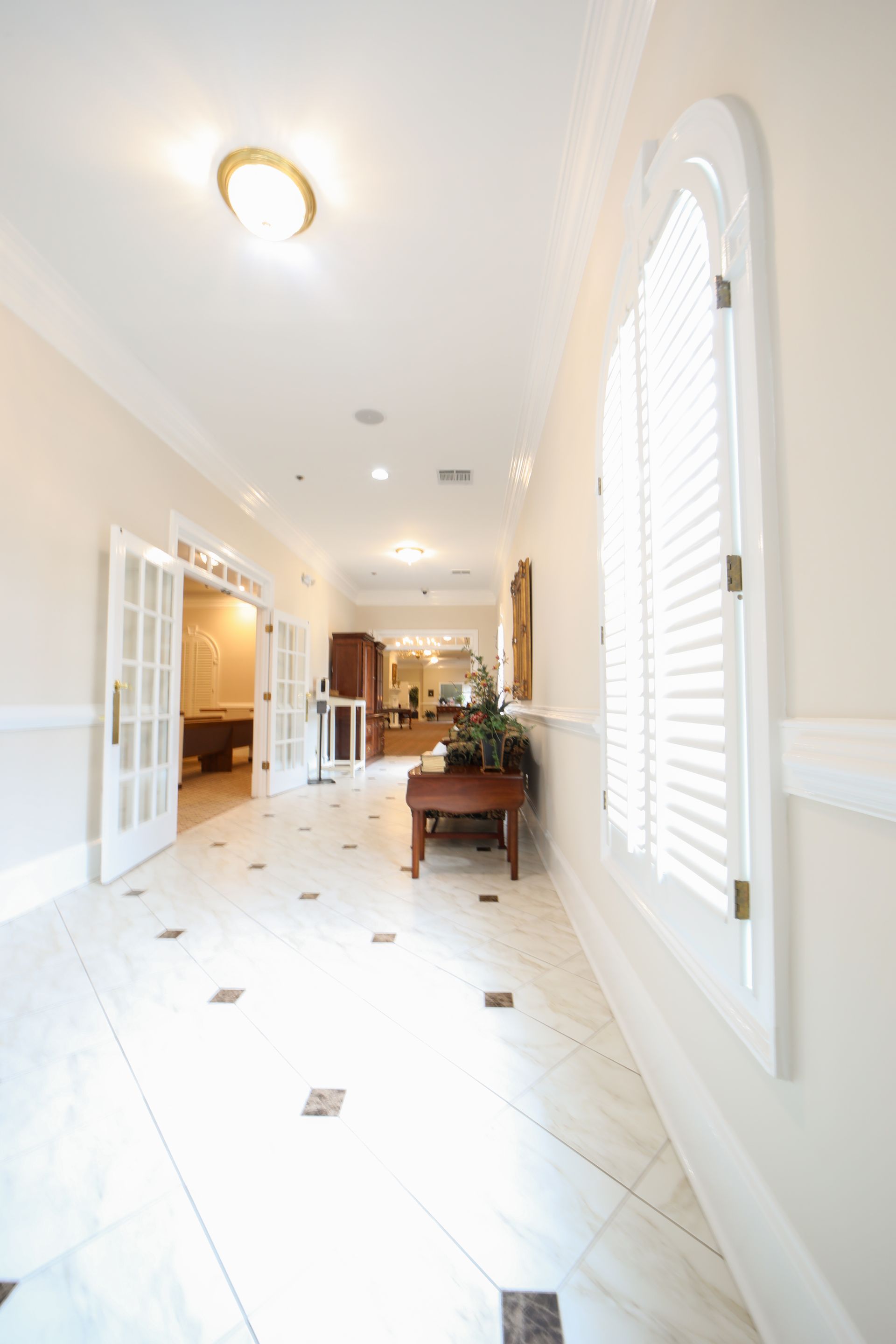 Bright hallway with white tile floors, arched windows, and a small table near the far end