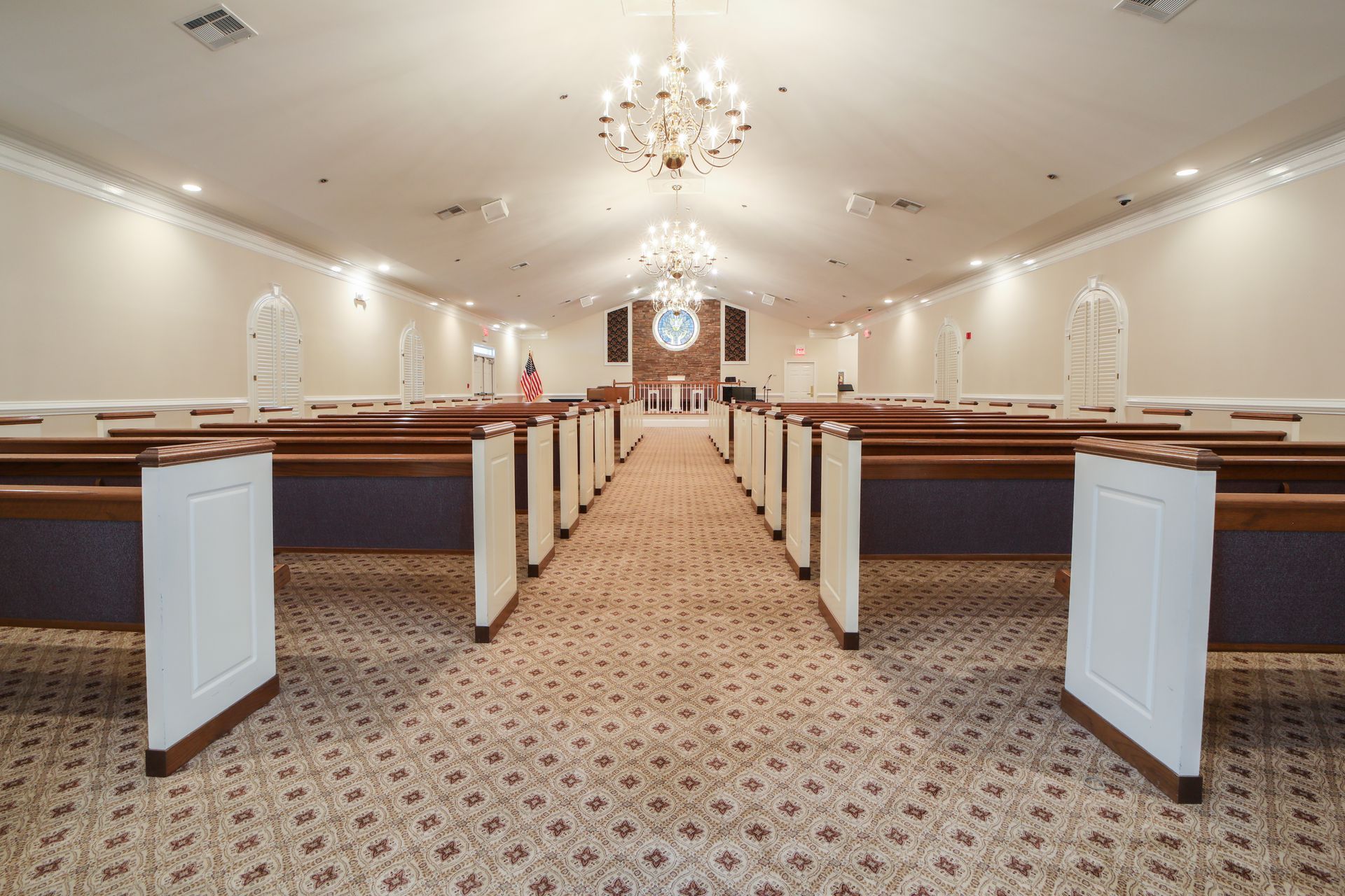 Empty wedding chapel aisle with white pews, chandeliers, and carpeted floor