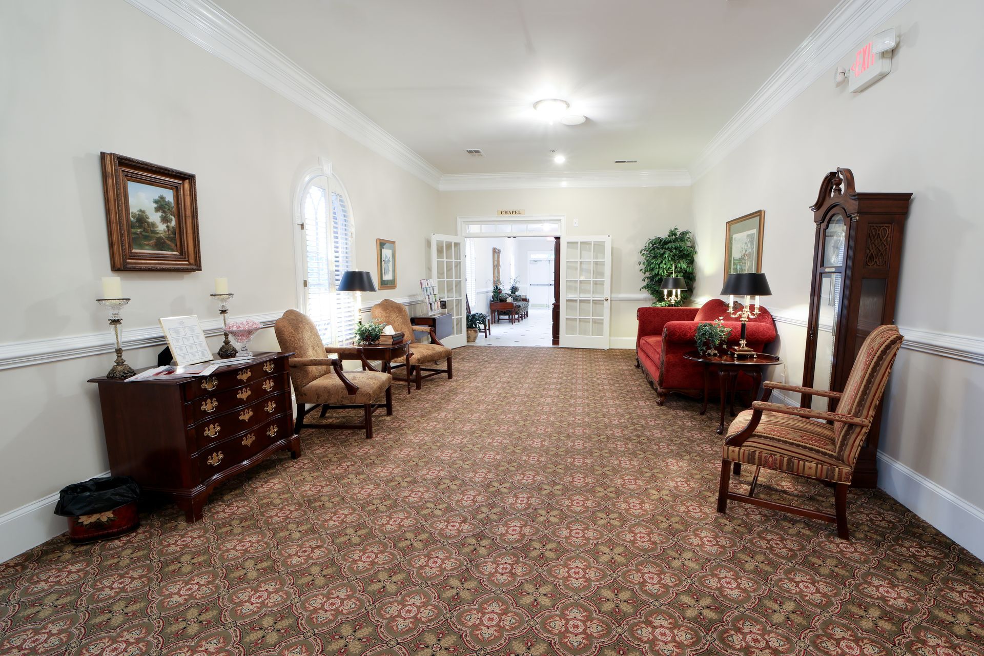 Spacious room with patterned carpet, chairs, red sofa, and tall wooden cabinets along cream walls.