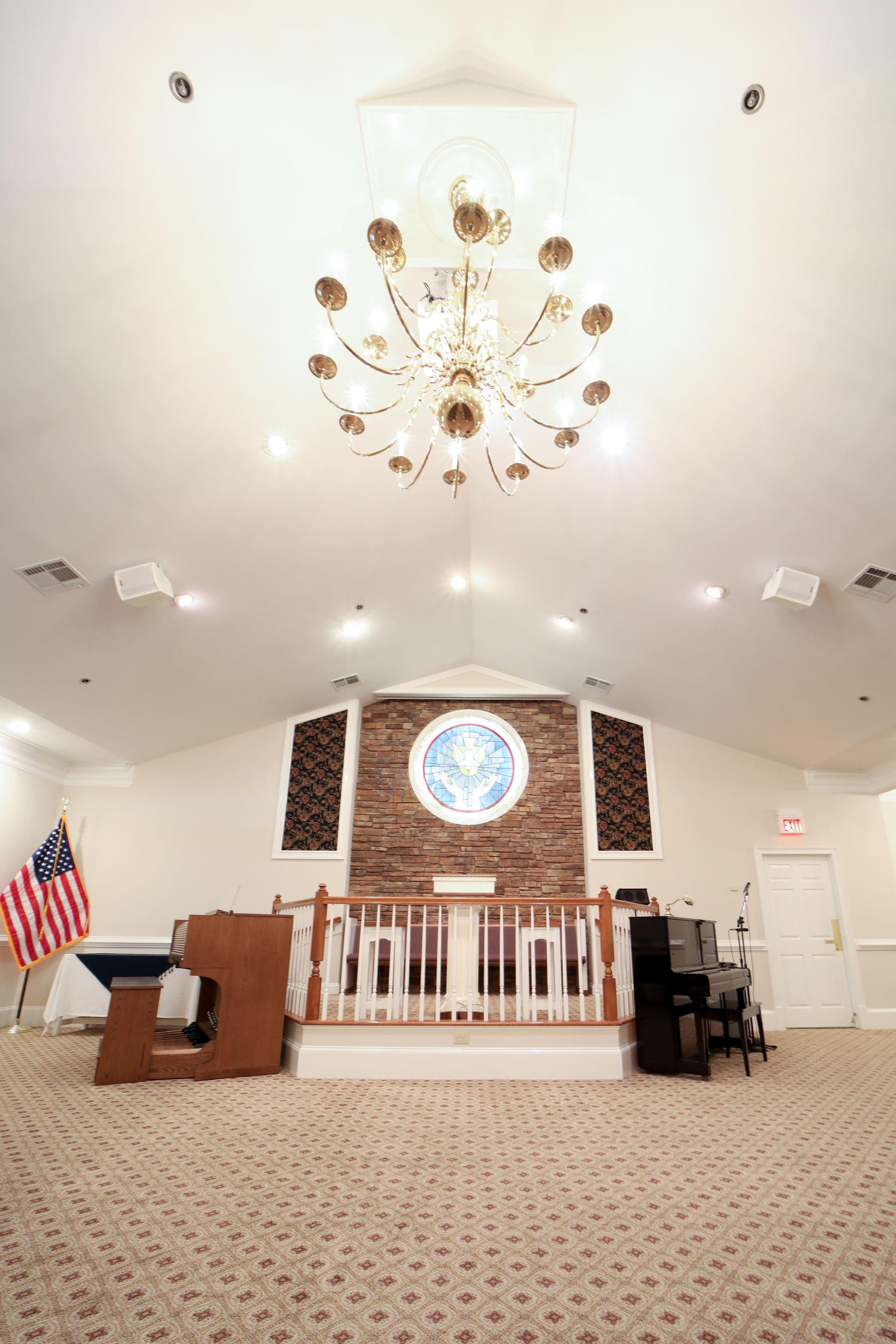 Church sanctuary with white ceiling, chandelier, altar, brick wall, and American flag beside the pulpit.