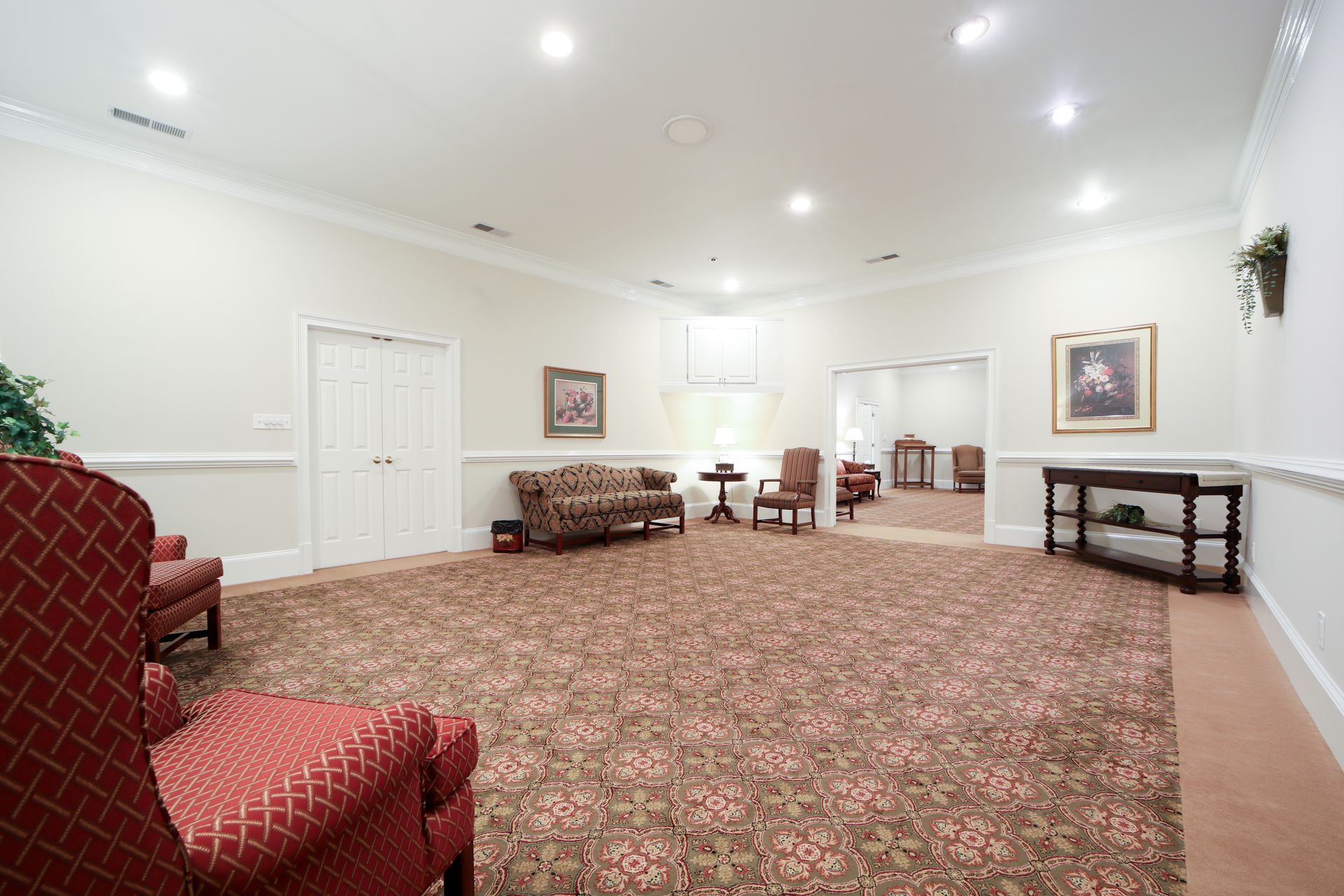 Bright, empty lobby with patterned carpet, white walls, chairs, and framed artwork.