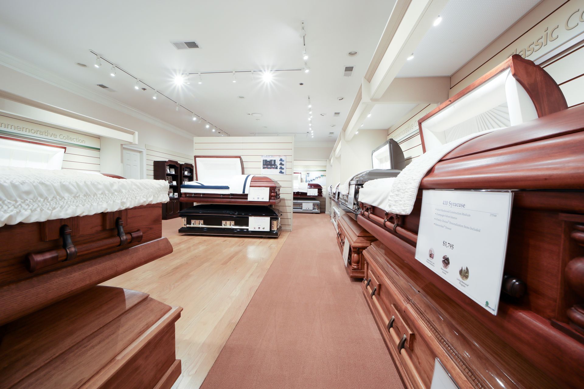 Wooden coffins displayed in a bright funeral showroom with carpeted aisle and white ceiling lights
