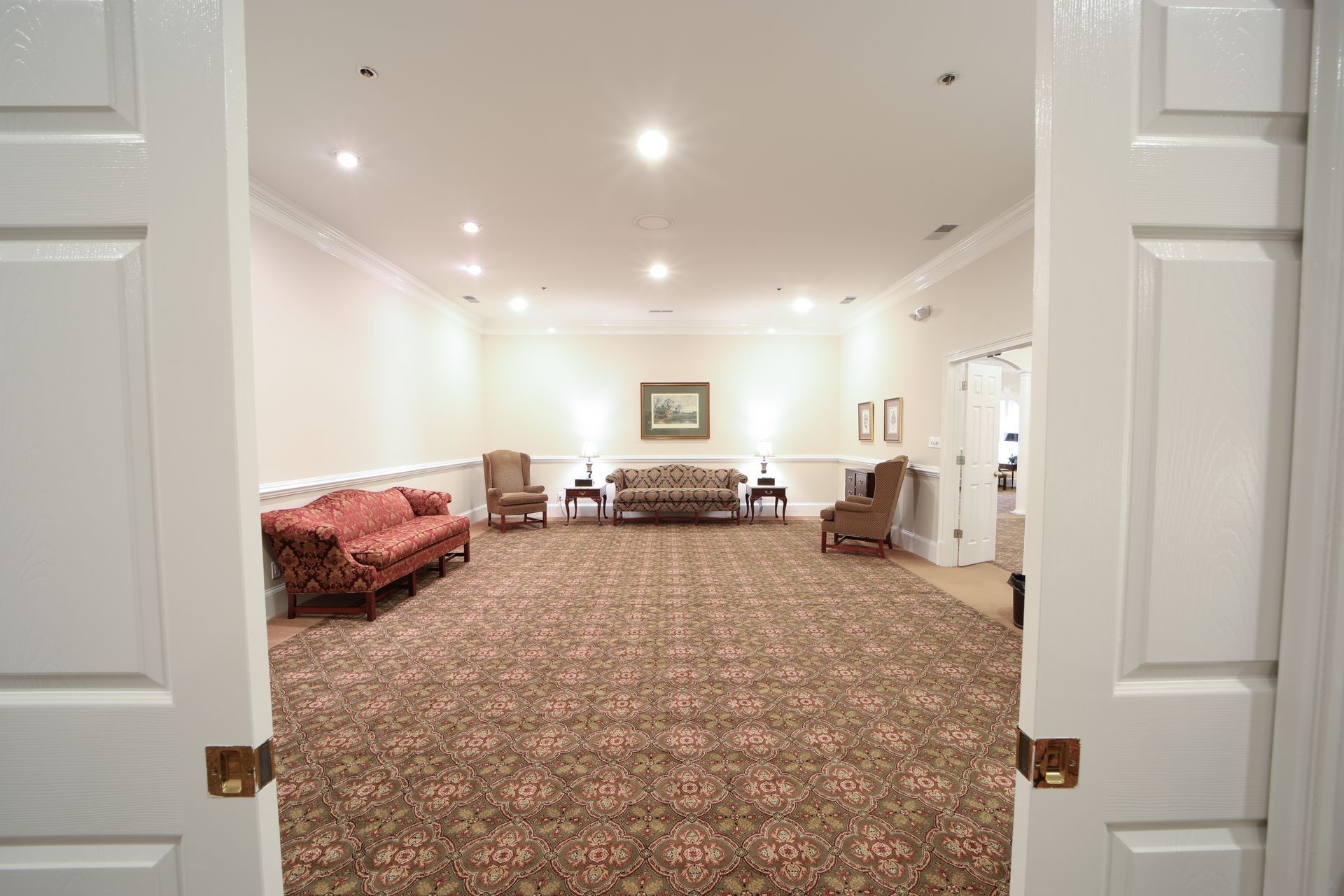 Bright carpeted lobby with white walls, recessed lights, benches, and a couch, viewed through open double doors