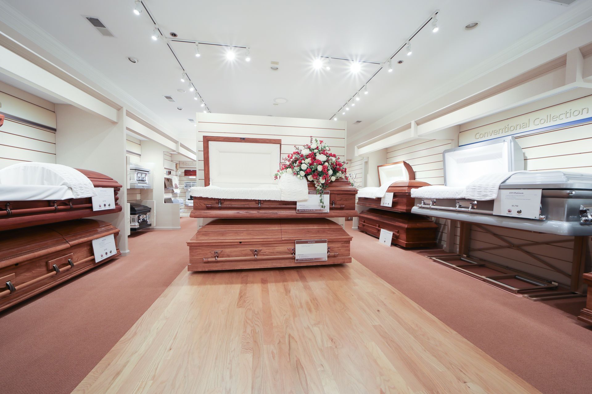 Bright showroom with polished wooden caskets and floral arrangements under white ceiling lights