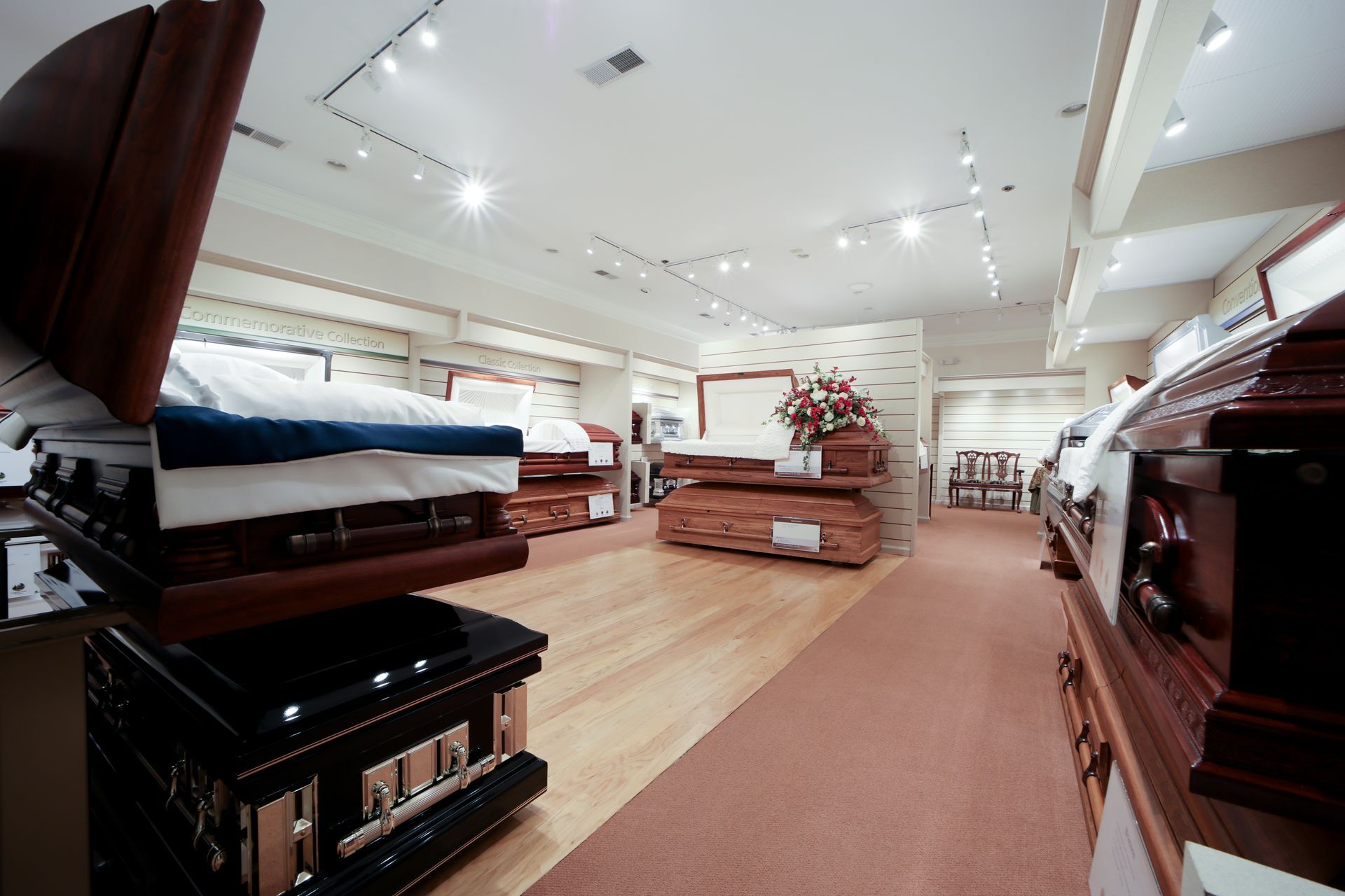 Wide casket showroom with beds, sofas, and wooden display pieces under bright ceiling lights
