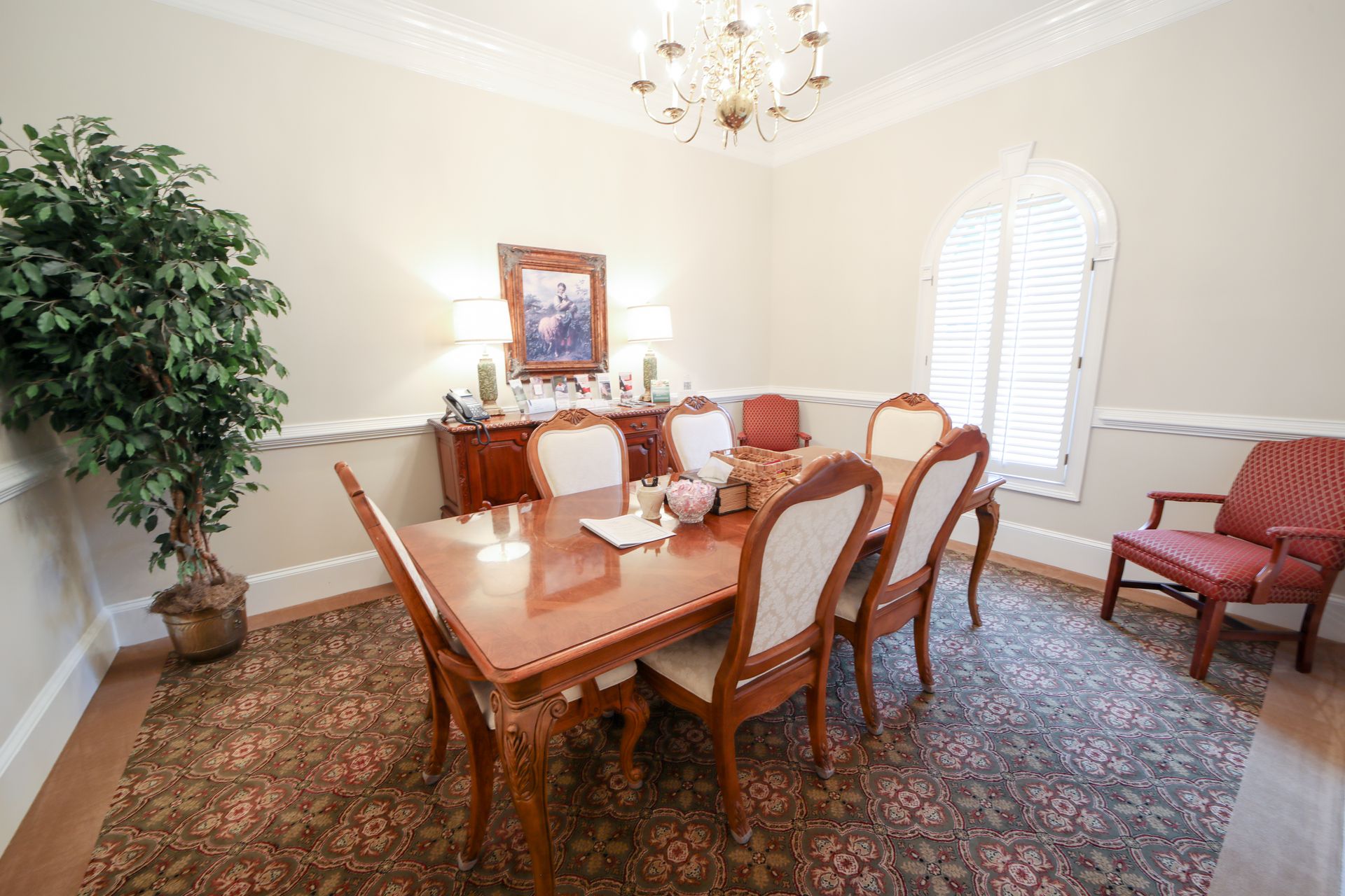 Elegant room with wooden table, upholstered chairs, chandelier, and patterned carpet near a window