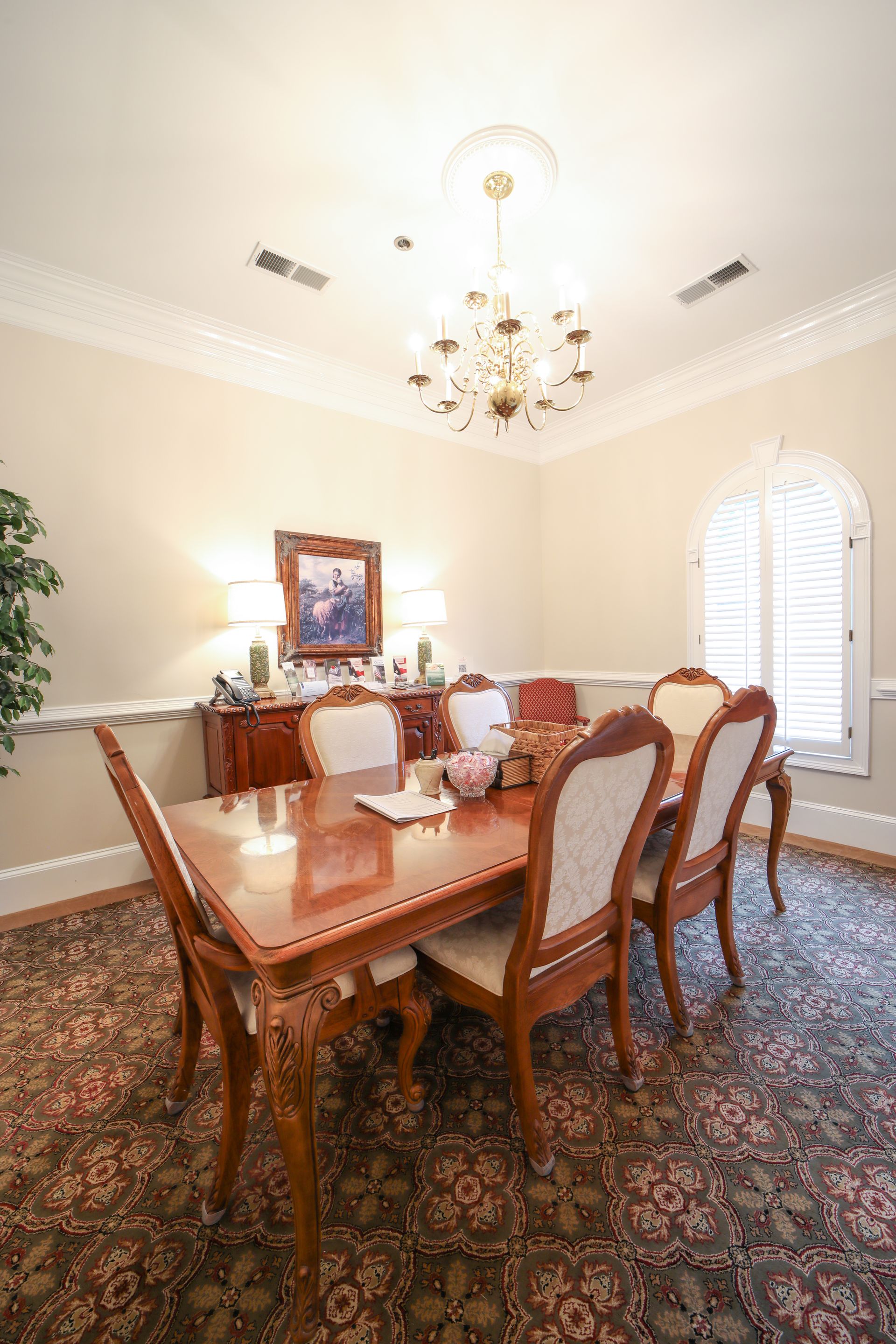Formal dining room with wooden table, upholstered chairs, chandelier, and framed art on cream walls.