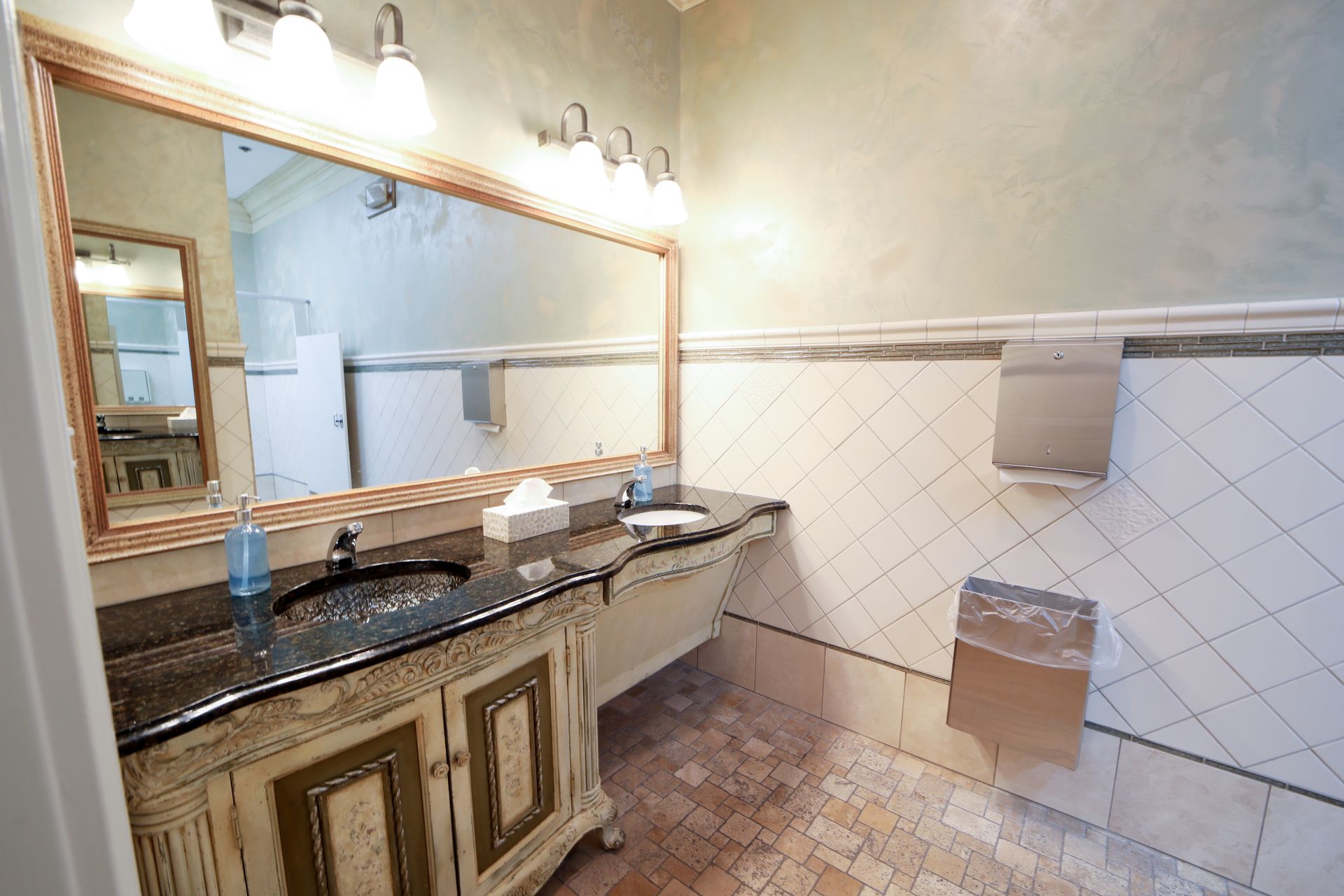 Bathroom with large mirror, granite vanity, wall tiles, and toilet paper dispensers