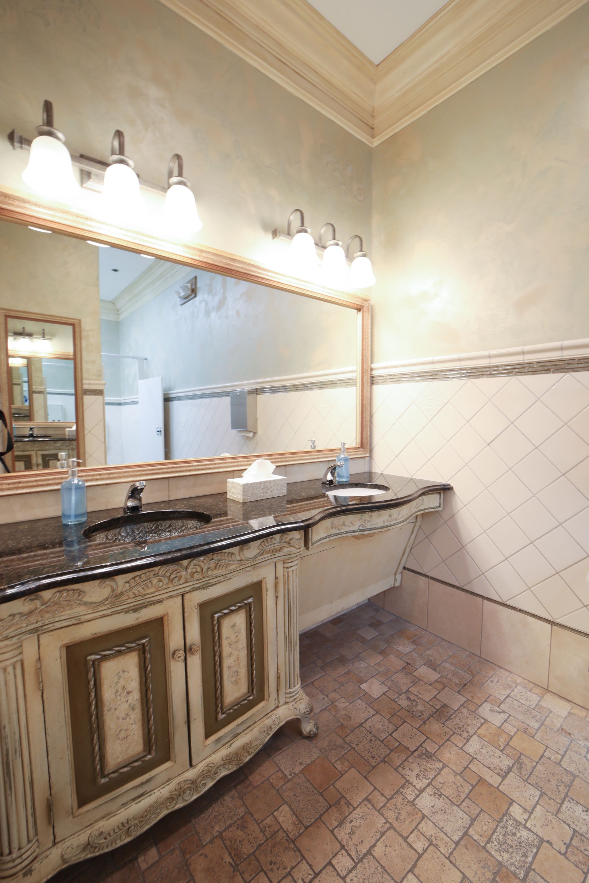 Elegant bathroom vanity with large mirror, granite countertop, and cream tile walls and floor.