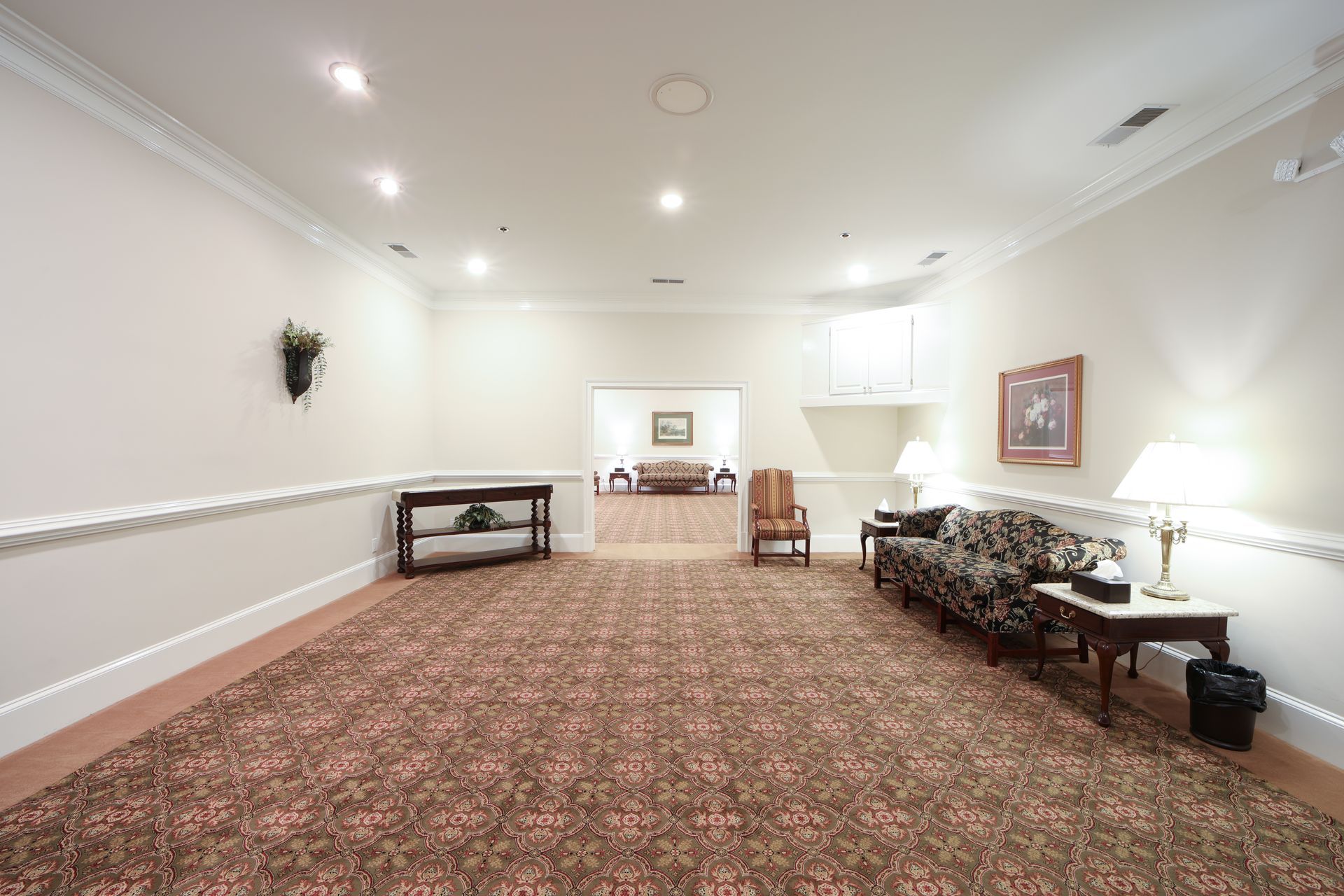 Spacious carpeted room with white walls, recessed lights, and sofas along the right wall.