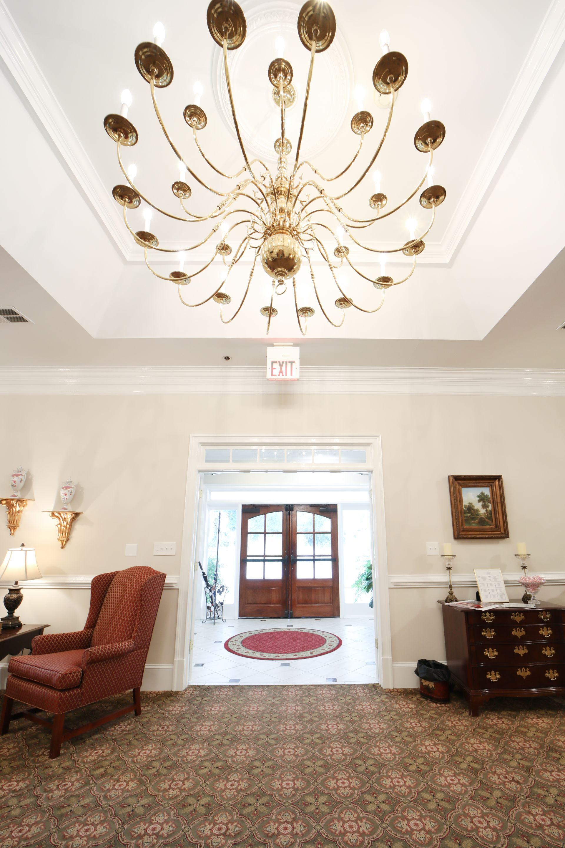 Elegant lobby with gold chandelier, patterned carpet, and double doors leading outside.