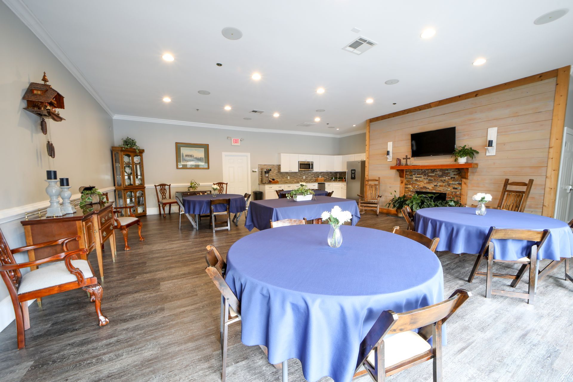 room with round tables draped in blue cloths, wooden chairs, and a fireplace in the background
