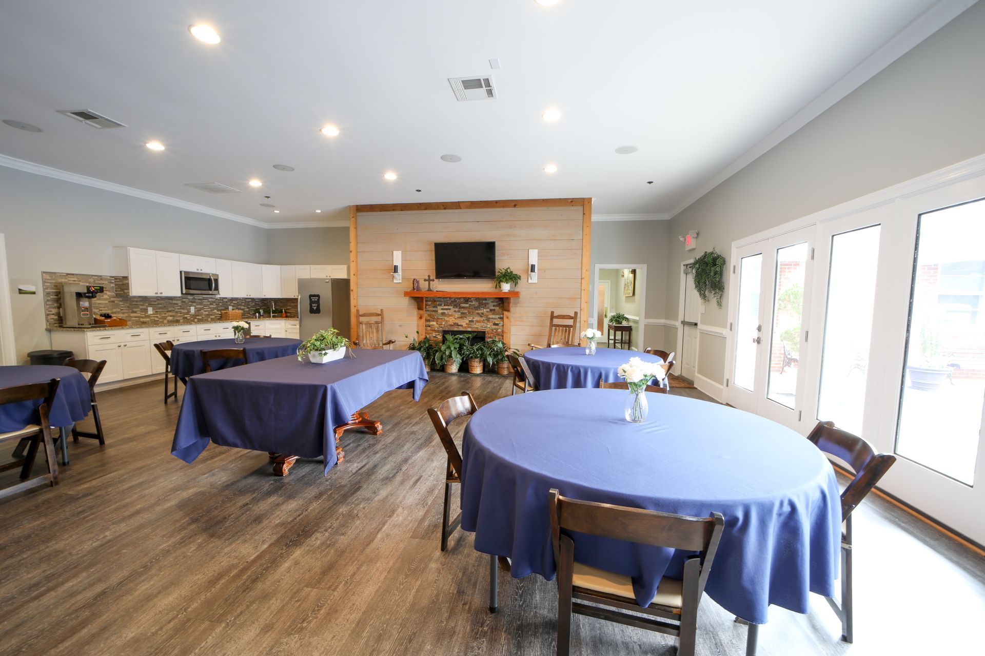 Bright room with round blue tablecloth tables, wooden floor, fireplace, and large windows