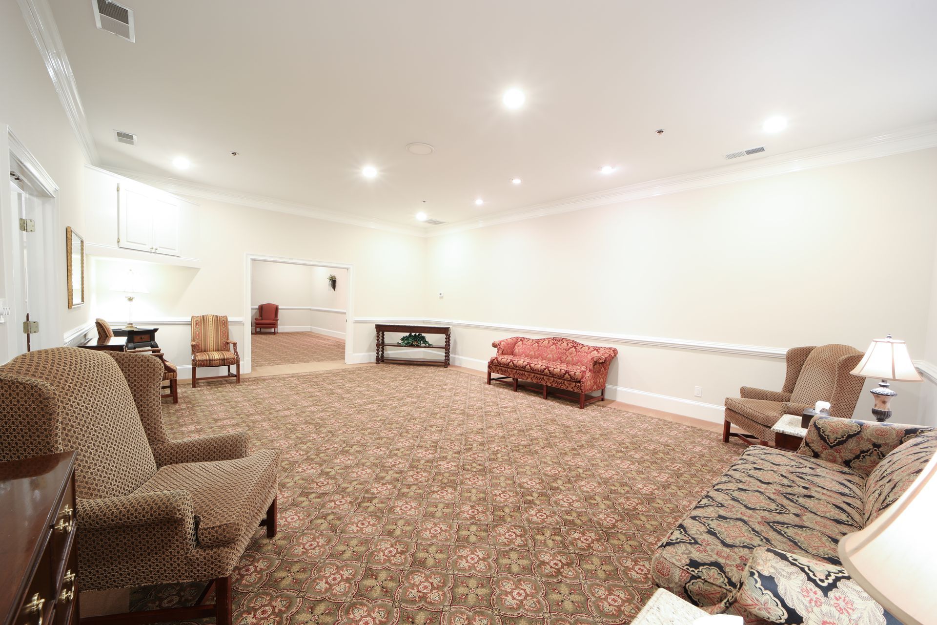 Spacious carpeted room with upholstered chairs, a sofa, lamps, and a fireplace against white walls.