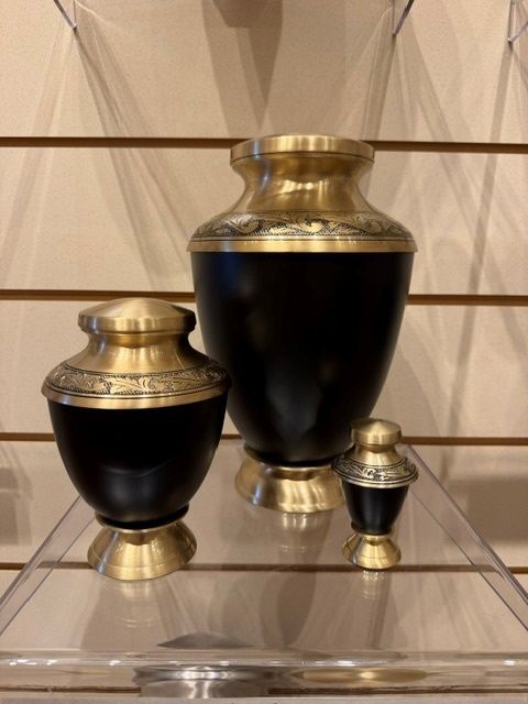 Three black and gold decorative urns displayed on a clear glass shelf.