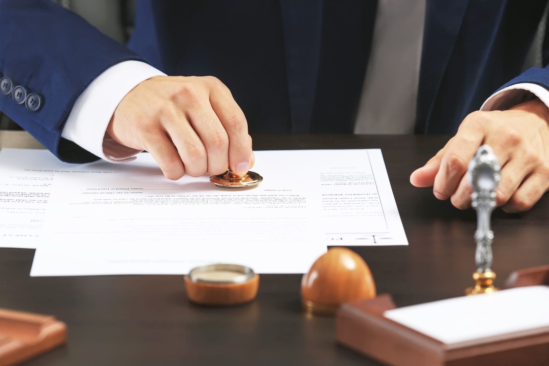 Hands signing a document at a desk with a gavel and stamp, suggesting a legal agreement