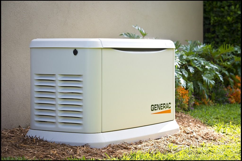 Outdoor white backup generator beside a house wall, with vents and a grassy yard nearby
