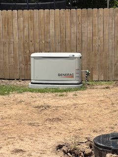 Generac backup generator beside a wooden fence in a dirt yard
