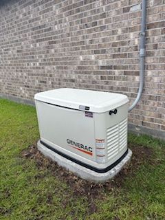 White Generac generator beside a brick house, connected by conduit on a concrete pad.