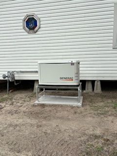 Gray generator unit on a metal platform beside a house with white siding and a round window.