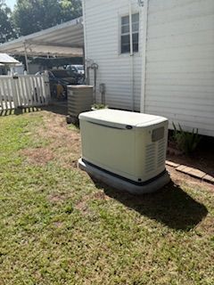 Portable generator beside a white house in a grassy yard, near a patio and fence.