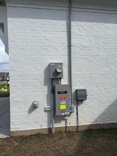 Electrical utility boxes and meter mounted on a white brick exterior wall.