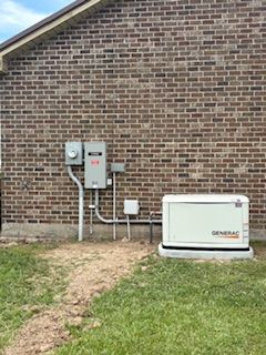Brick house exterior with electrical boxes and a white generator on the lawn