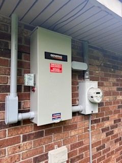 Electrical meter and breaker panel mounted on a brick house exterior under a covered eave.