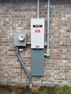 Electrical meter and breaker panel mounted on a brick exterior wall with gray conduit.