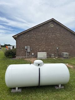 White horizontal propane tank on stands in front of a brick building outdoors.