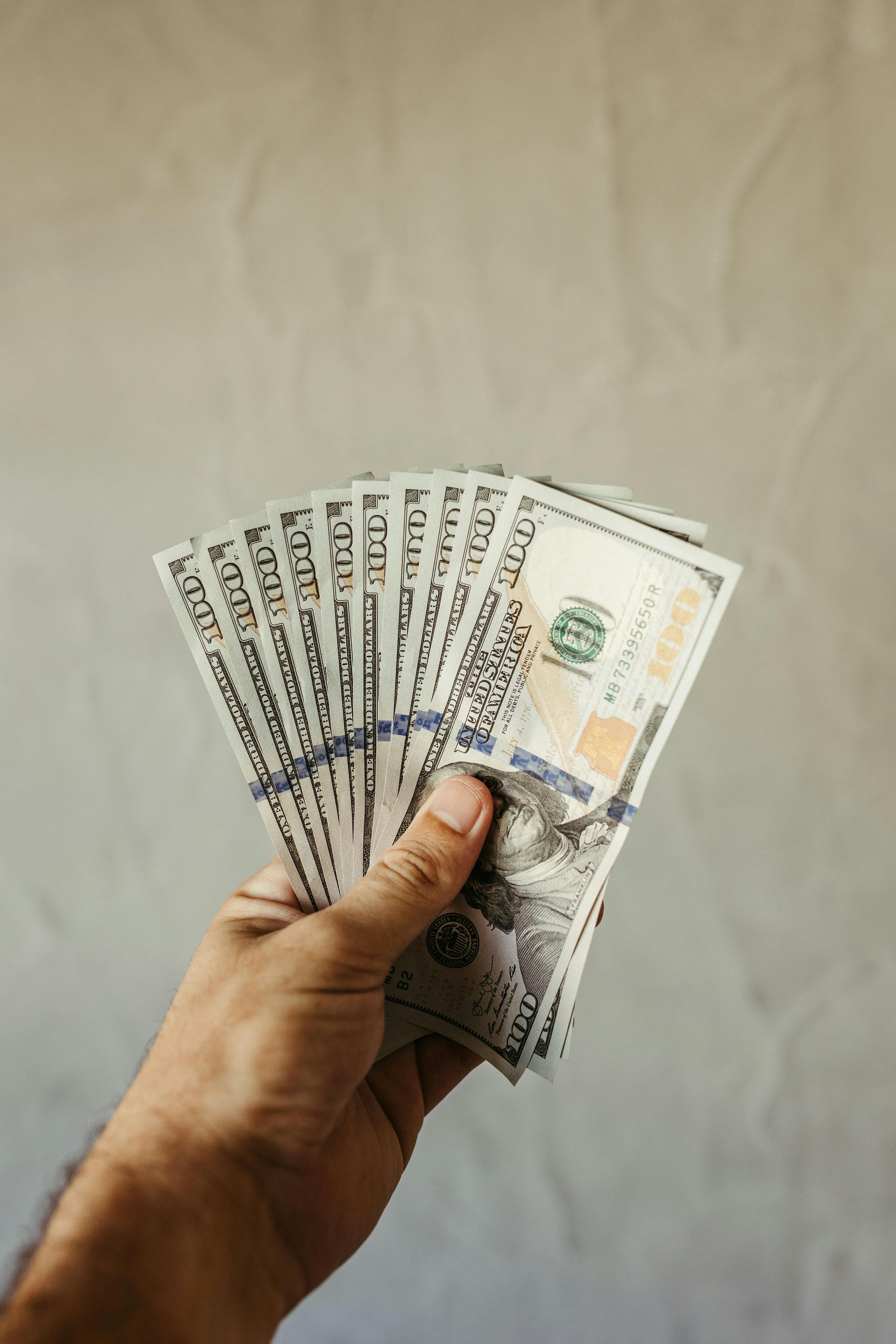 Hand holding fanned stacks of banknotes against a plain beige background