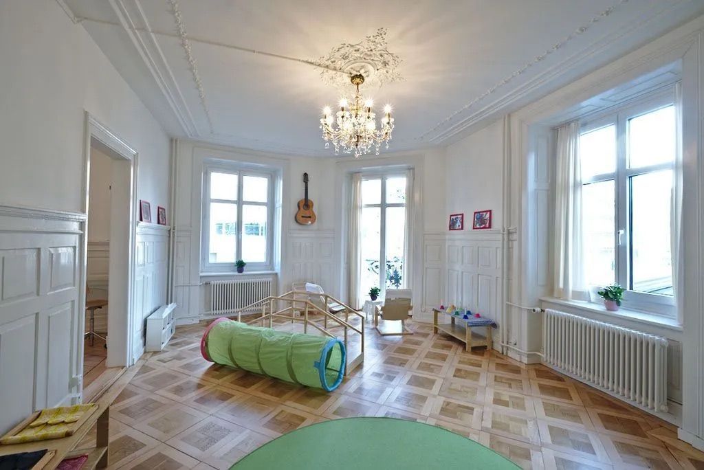 A living room with wooden floors , a green rug , a chandelier , and a guitar on the wall.