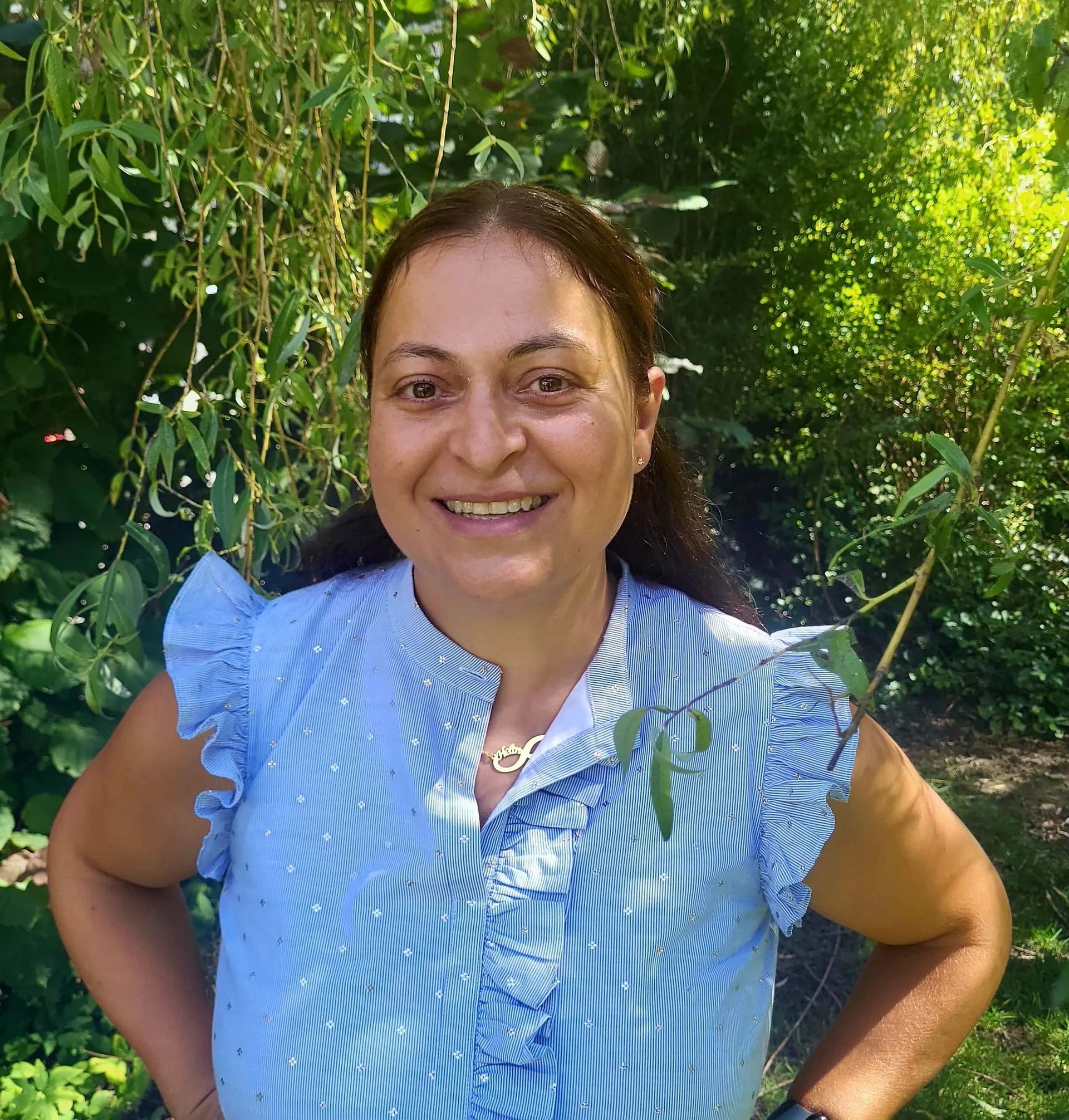 A woman in a blue striped shirt is smiling in front of a tree.