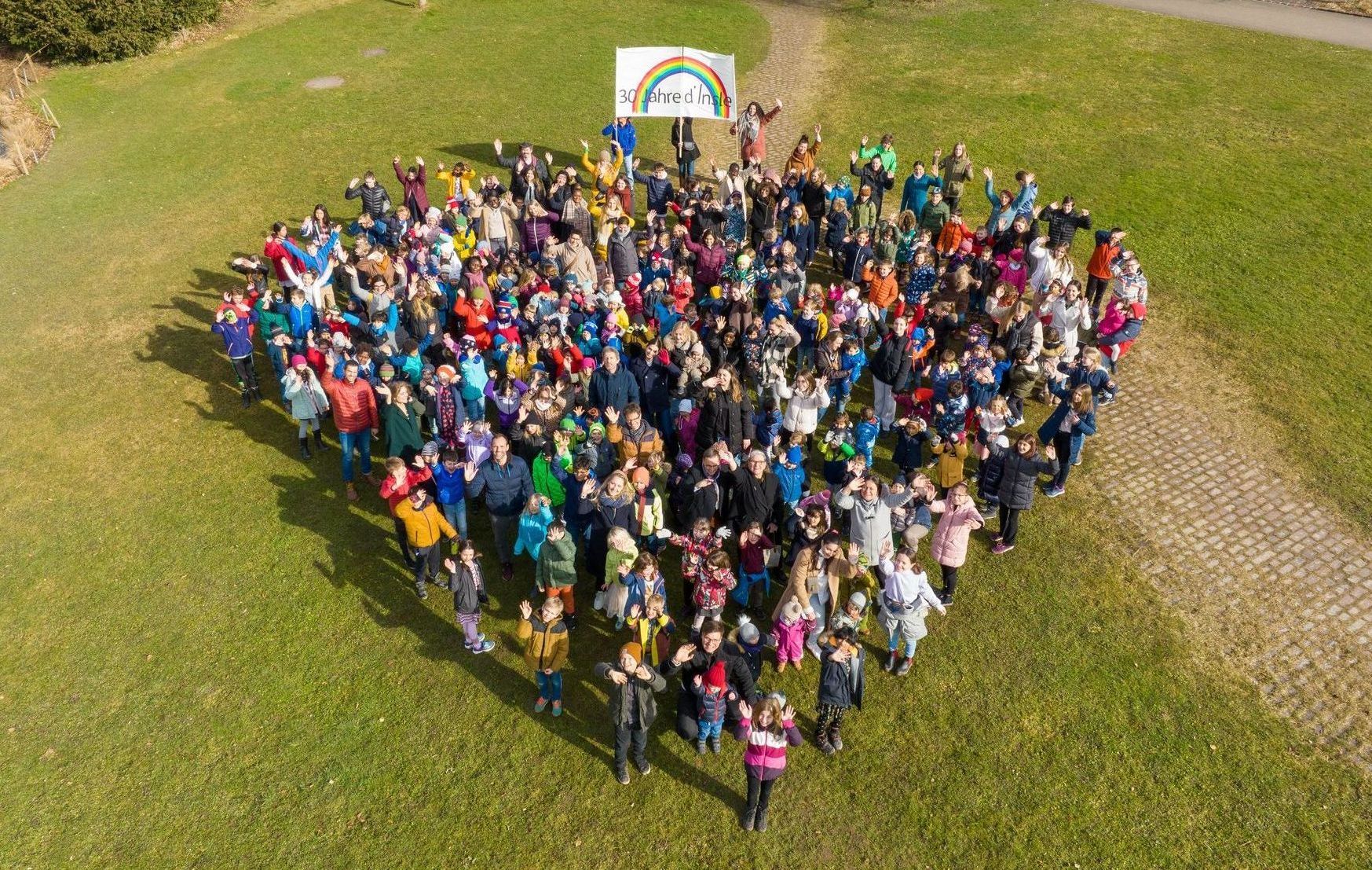 A large group of people are standing in a field in the shape of a heart.