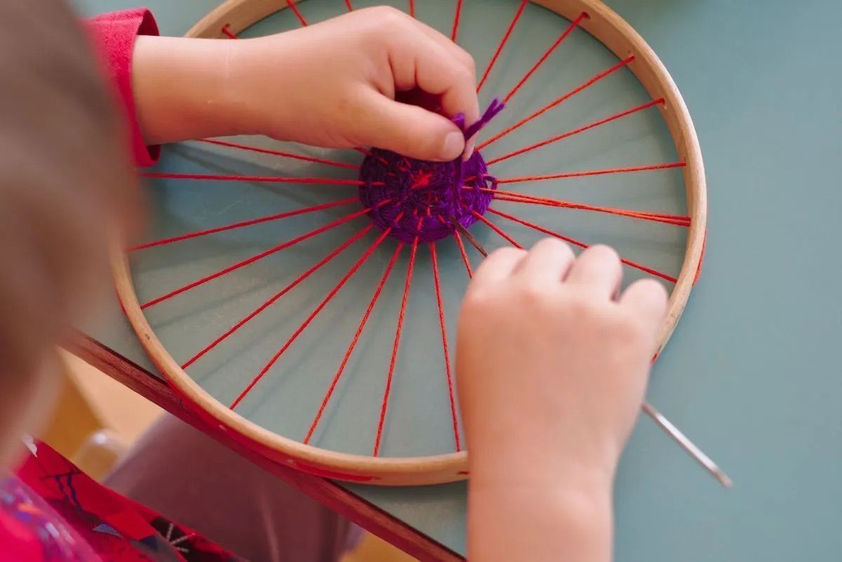 A child is weaving yarn on a circular loom