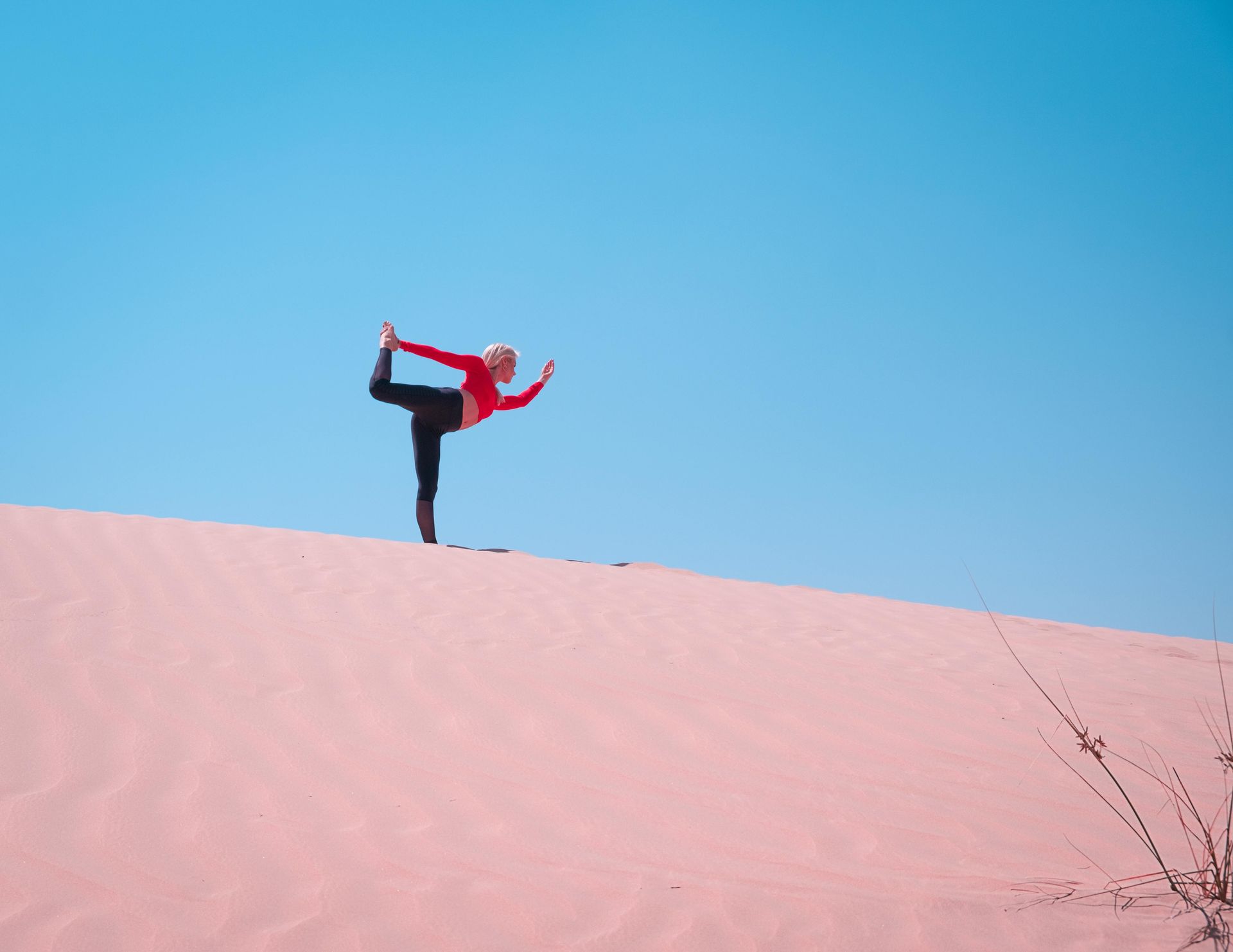A woman is doing yoga on top of a pink sand dune.