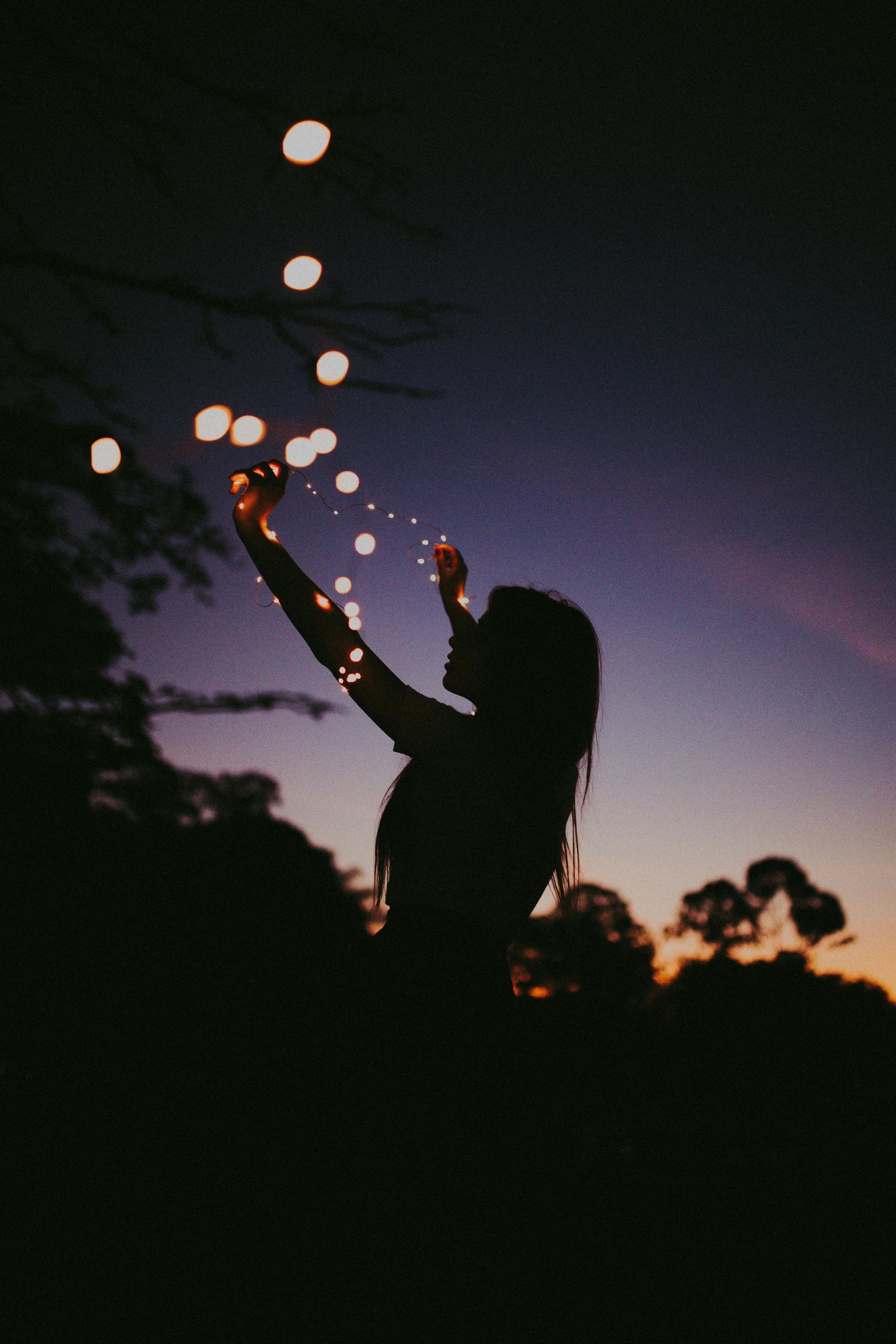 A silhouette of a woman holding a string of lights at night.