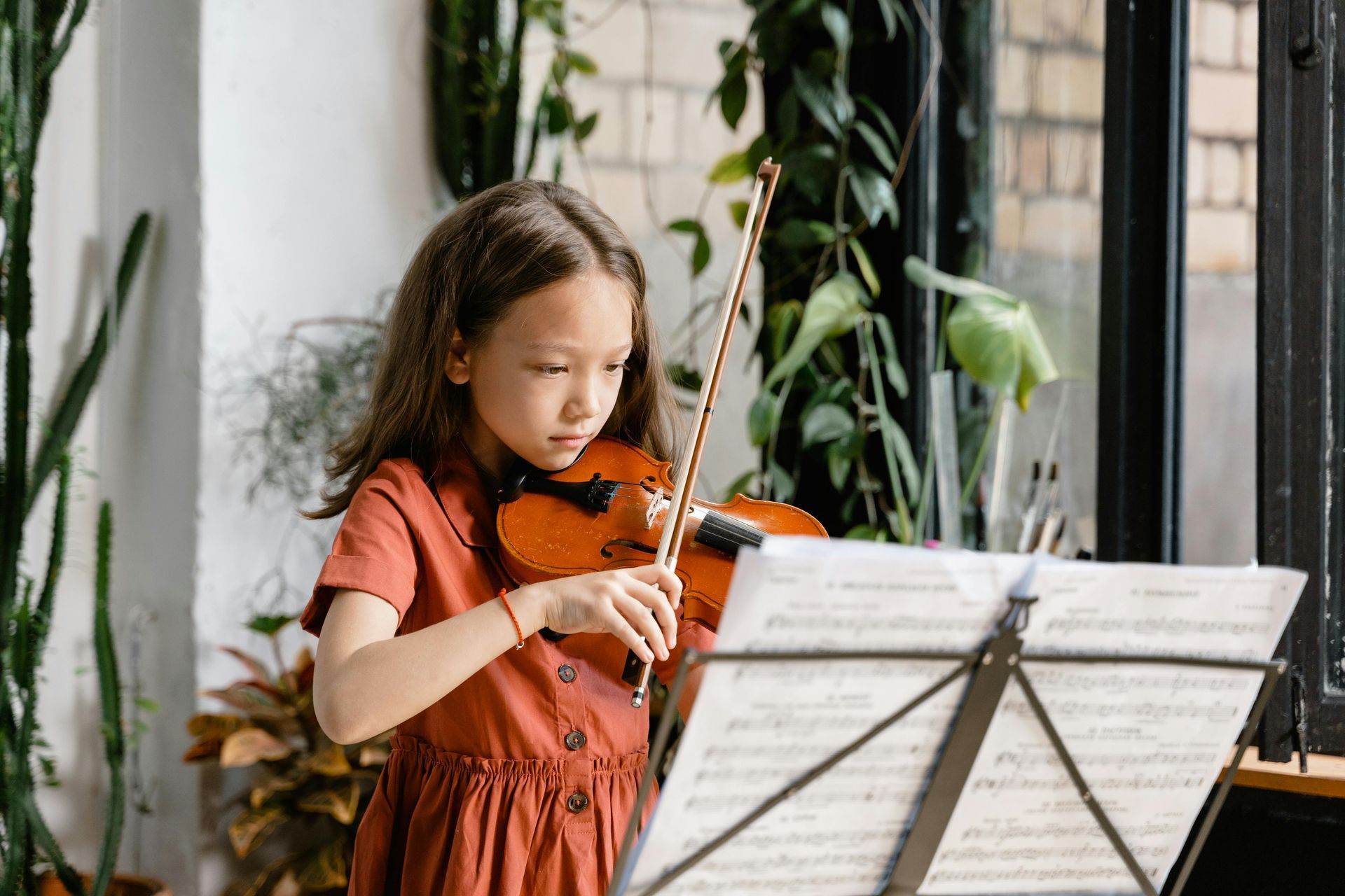 A young girl is playing a violin in front of a music stand.