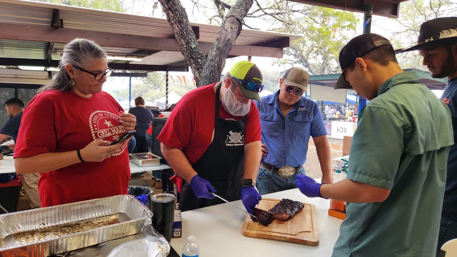 GGC team members preparing food at the San Antonio Engineering BBQ Cook-off, wearing gloves, with trays and cut meat.