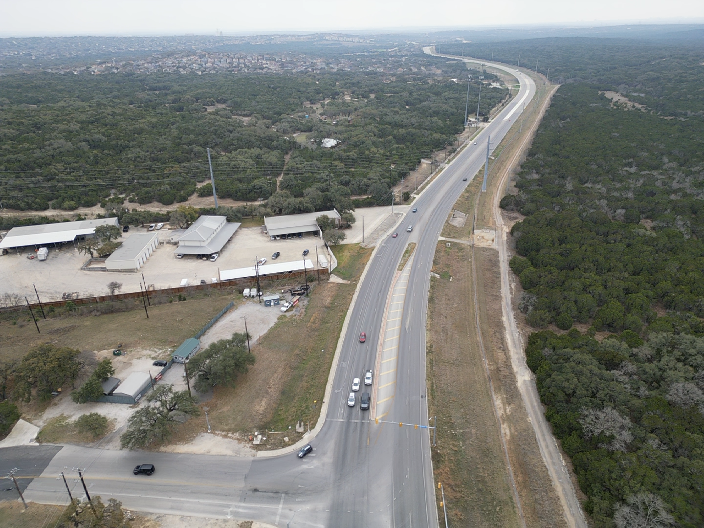 Aerial view of a long straight road through a suburban neighborhood with scattered houses and open lots.